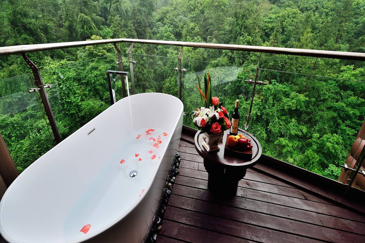 Une baignoire sur une terrasse en bois, avec vue sur une forêt dense.