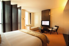 A hotel room with a large bed, a sofa, a TV, and a small table with a vase and fruit. - Beijing Hotel MOMC (Beijing)