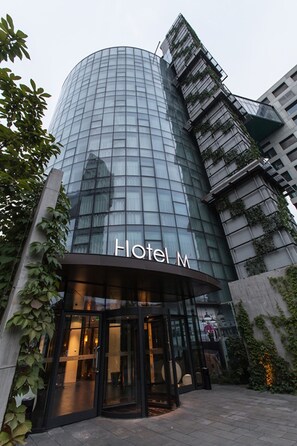 A modern hotel with a curved glass facade and the name "Hotel M" displayed prominently. - Beijing Hotel MOMC (Beijing)