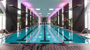 A long indoor swimming pool with a wooden deck in the foreground, surrounded by dark vertical panels and large windows. - Beijing Hotel MOMC (Beijing)