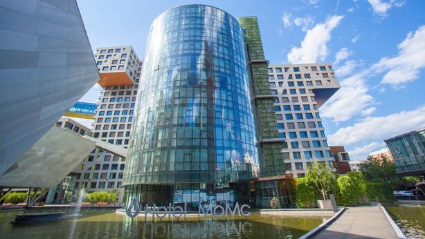 A modern hotel with a glass facade, surrounded by other contemporary buildings and a water feature. - Beijing Hotel MOMC (Beijing)