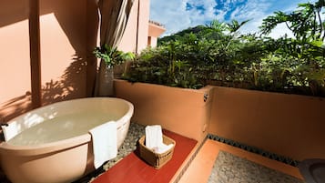 Un área de spa con una bañera grande, una mesita y una cesta de toallas.