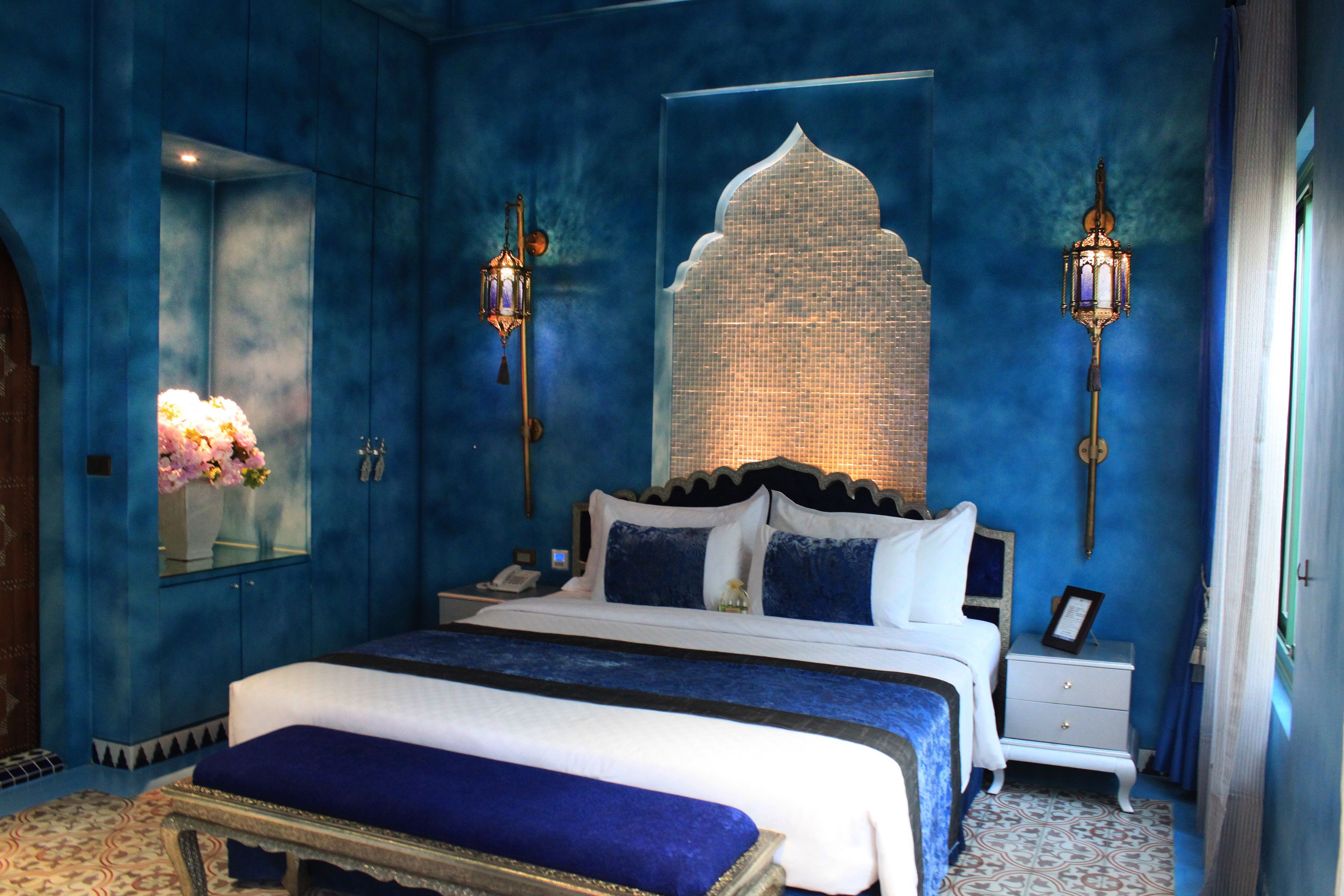 A bedroom with a large bed, two bedside tables, a nightstand, a mirror, and two wall-mounted lamps.