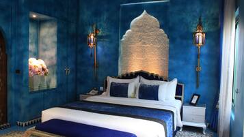 A bedroom with a large bed, two bedside tables, a nightstand, a mirror, and two wall-mounted lamps.