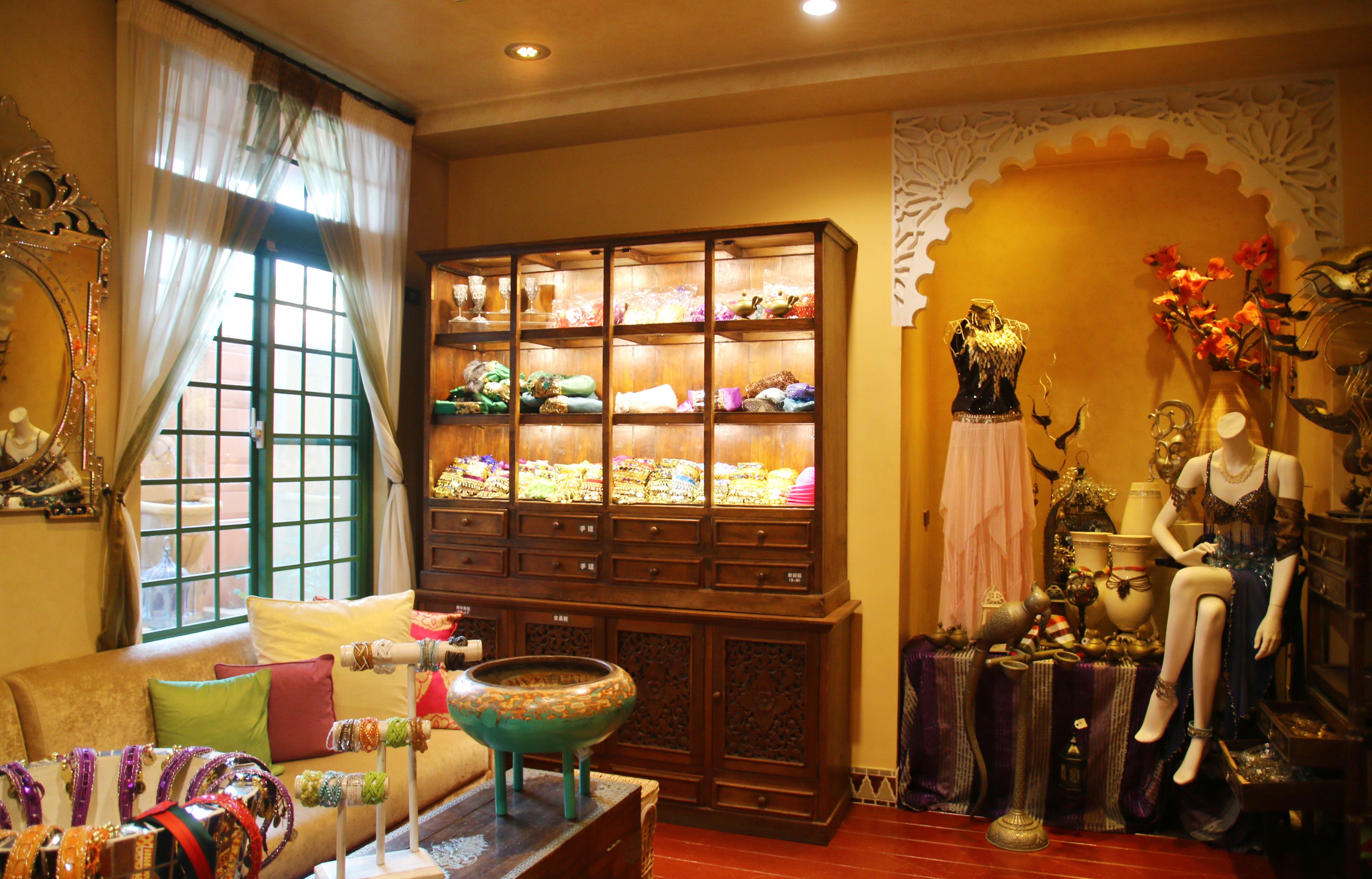 A boutique hotel room with a large wooden cabinet filled with textiles, a mannequin dressed in a gown, and a vintage-style lamp.