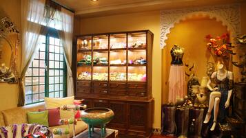 A boutique hotel room with a large wooden cabinet filled with textiles, a mannequin dressed in a gown, and a vintage-style lamp.