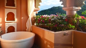 A bathroom with a freestanding bathtub, a window with a view of a mountain, and a planter with flowers. - Amanda Hotel Kenting (Hengchun)