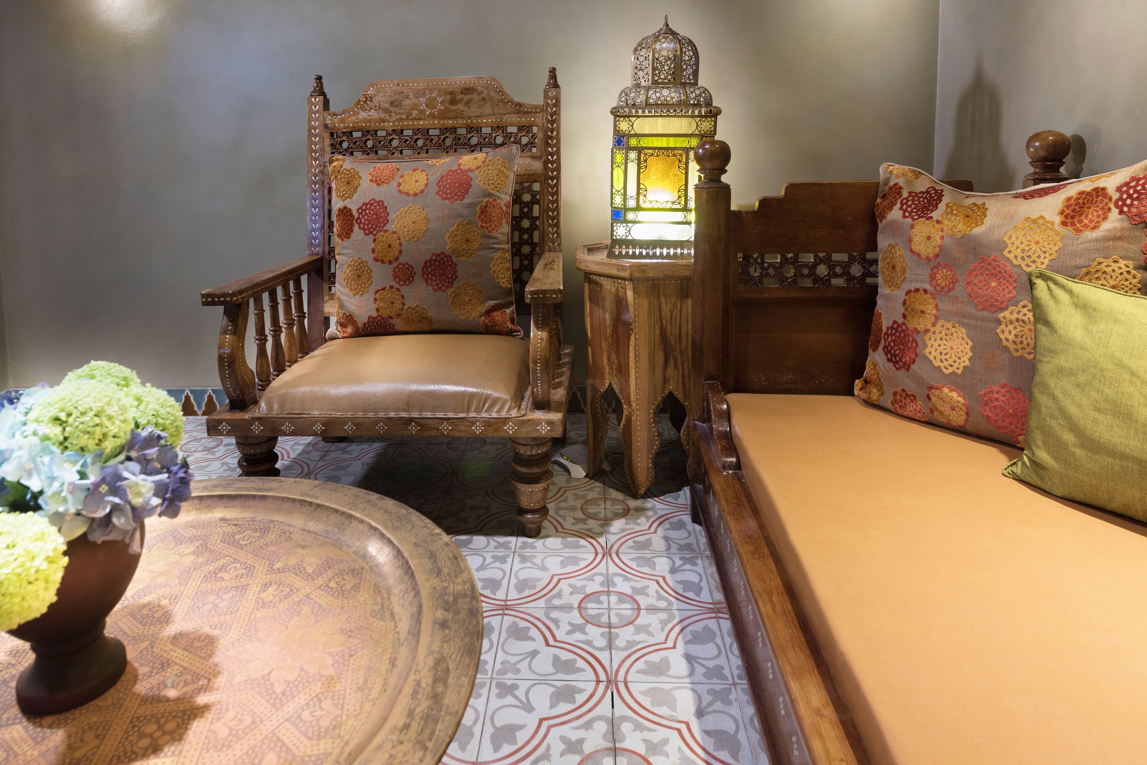Una habitación tradicional con una cama de madera, un sofá estampado, una mesita con un farol y un jarrón decorativo.
