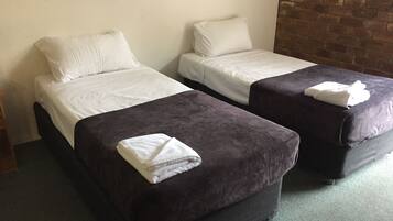A hotel room with two single beds, each with white linens and a dark-colored ottoman.