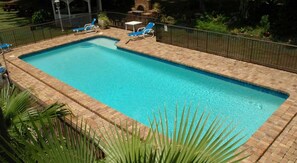 Una piscina rectangular con borde de ladrillo, rodeada por una cerca de metal.