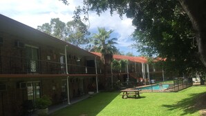 Un edificio de dos pisos con piscina, un patio cubierto y un césped bien cuidado.