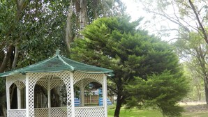 Un pabellón con techo verde y paredes de celosía, rodeado de árboles y césped.