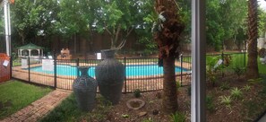 A backyard with a swimming pool, a gazebo, and a fenced area with palm trees and plants.