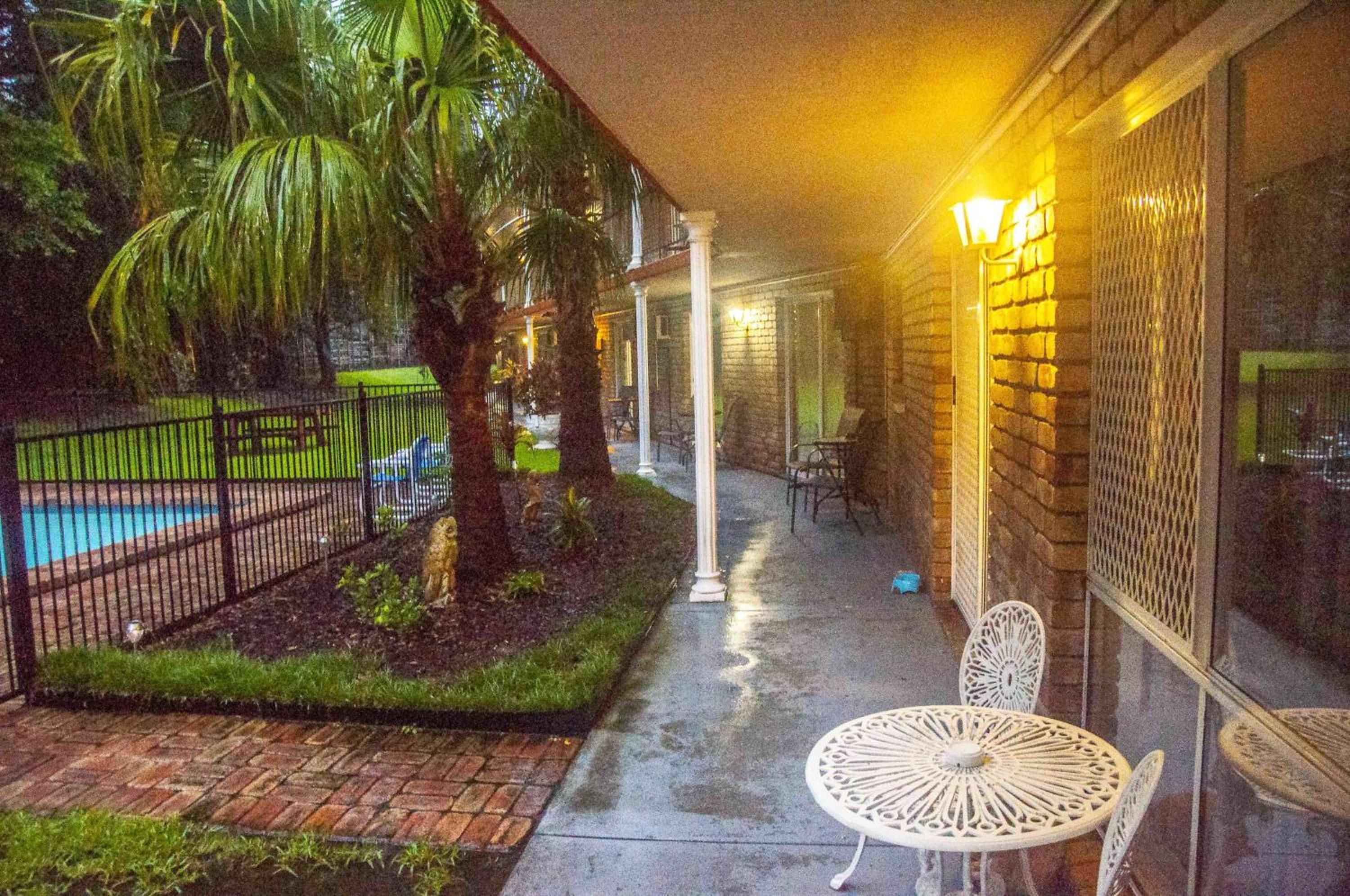 Un espacio exterior cubierto con un camino de ladrillo, una piscina, palmeras y una mesa y sillas blancas para exteriores.
