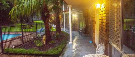 Un espacio exterior cubierto con un camino de ladrillo, una piscina, palmeras y una mesa y sillas blancas para exteriores.