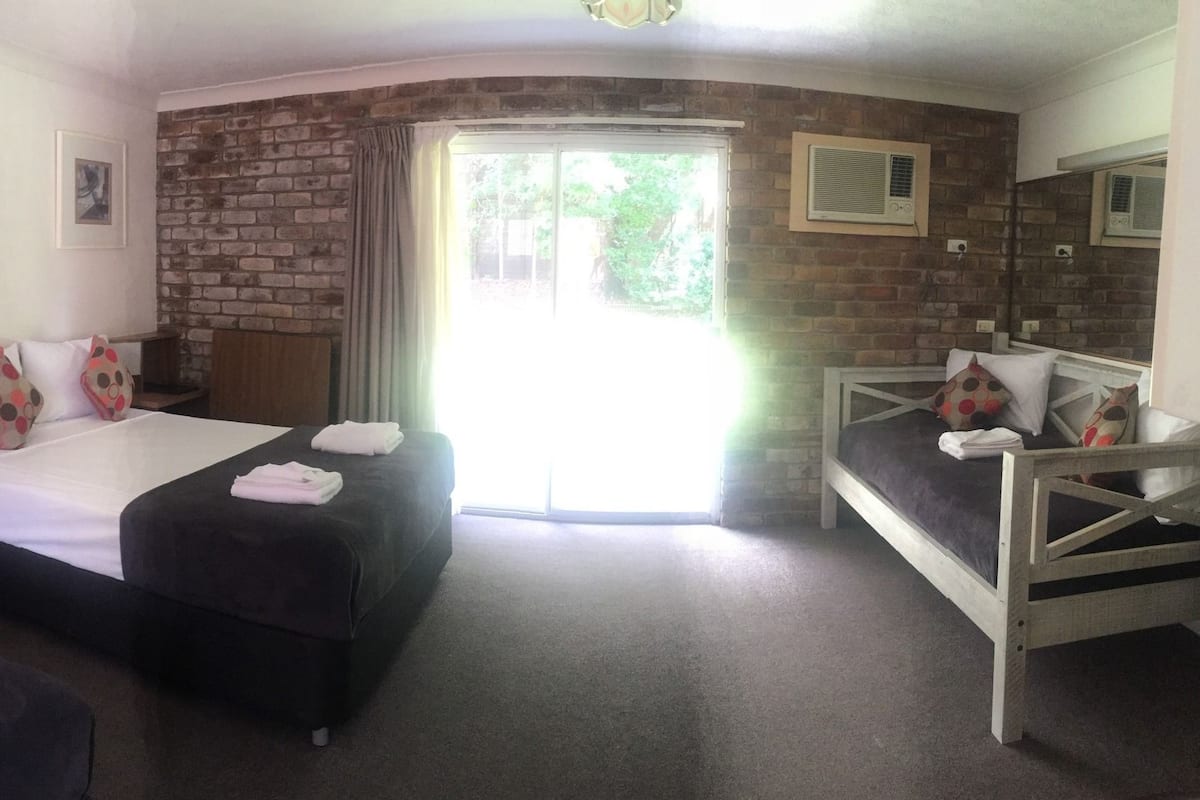 A hotel room with two beds, a brick wall, and a large window.