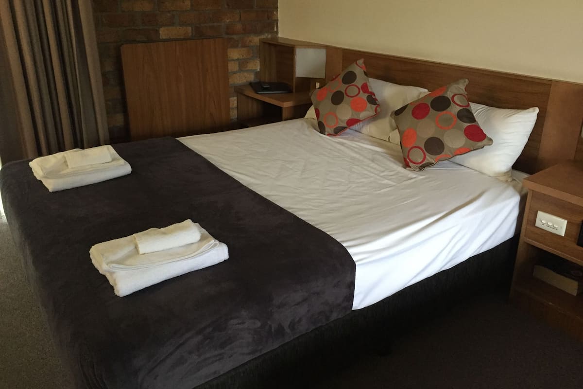 A neatly made bed with a dark headboard, white linens, and two decorative pillows with a polka dot pattern. There are two folded towels on the bed.