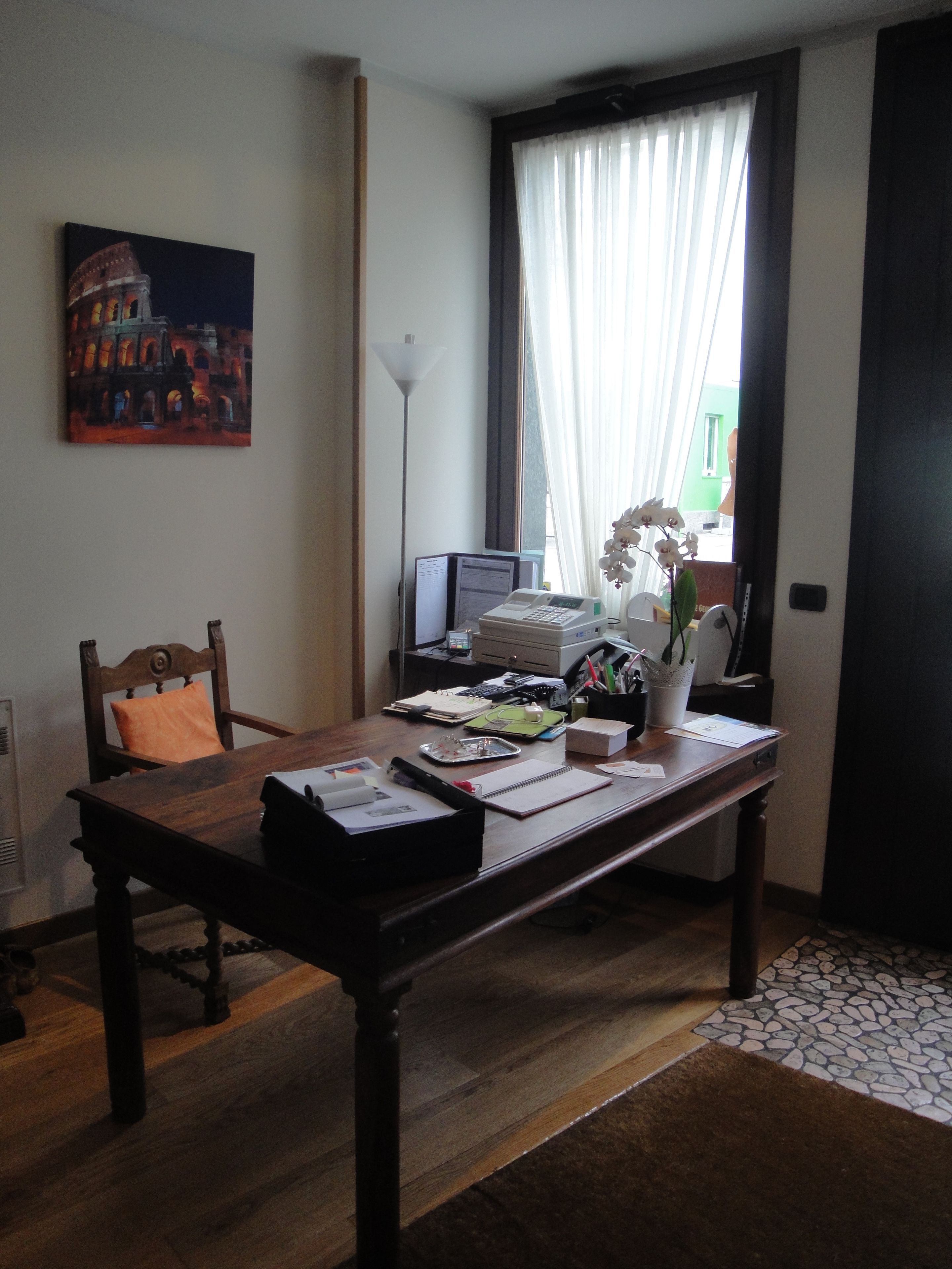 Une pièce avec un bureau en bois, une chaise, un tableau, une lampe et une fenêtre avec des rideaux.