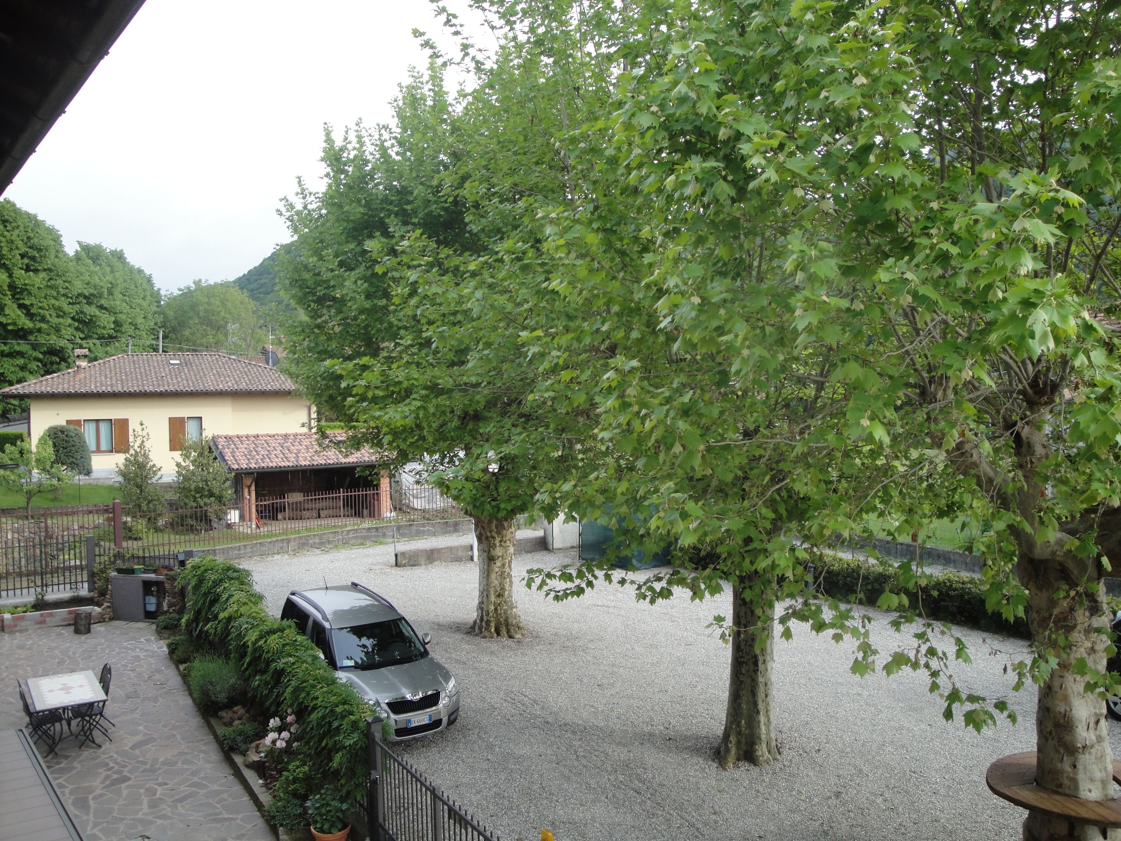 A courtyard with a gravel path, a parked car, a table and chairs, and a building with a tiled roof.