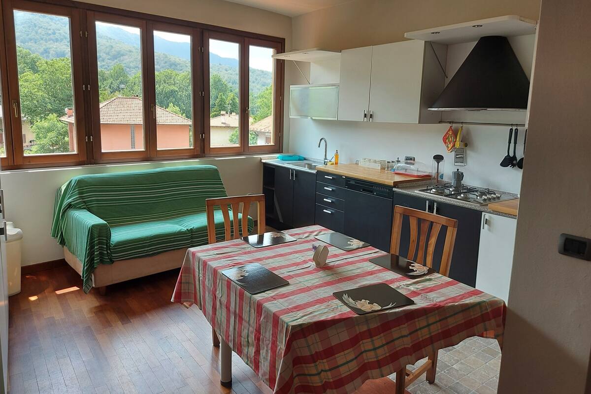 A compact kitchen with a dining area, a sofa, and a view of a mountainous landscape through large windows.