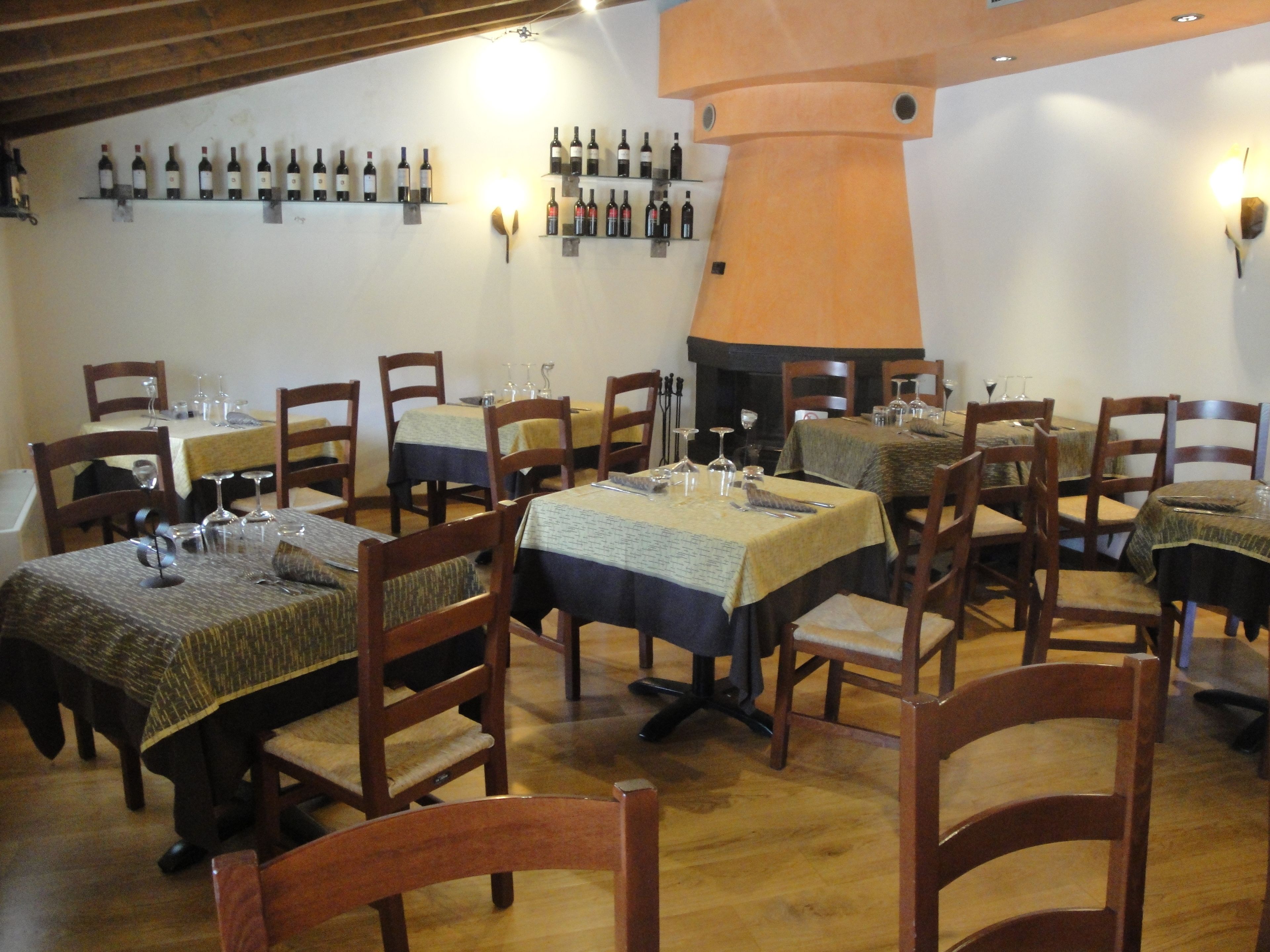 Ein Restaurant mit mehreren Tischen und Stühlen, Weinflaschen an der Wand und einem Kamin.