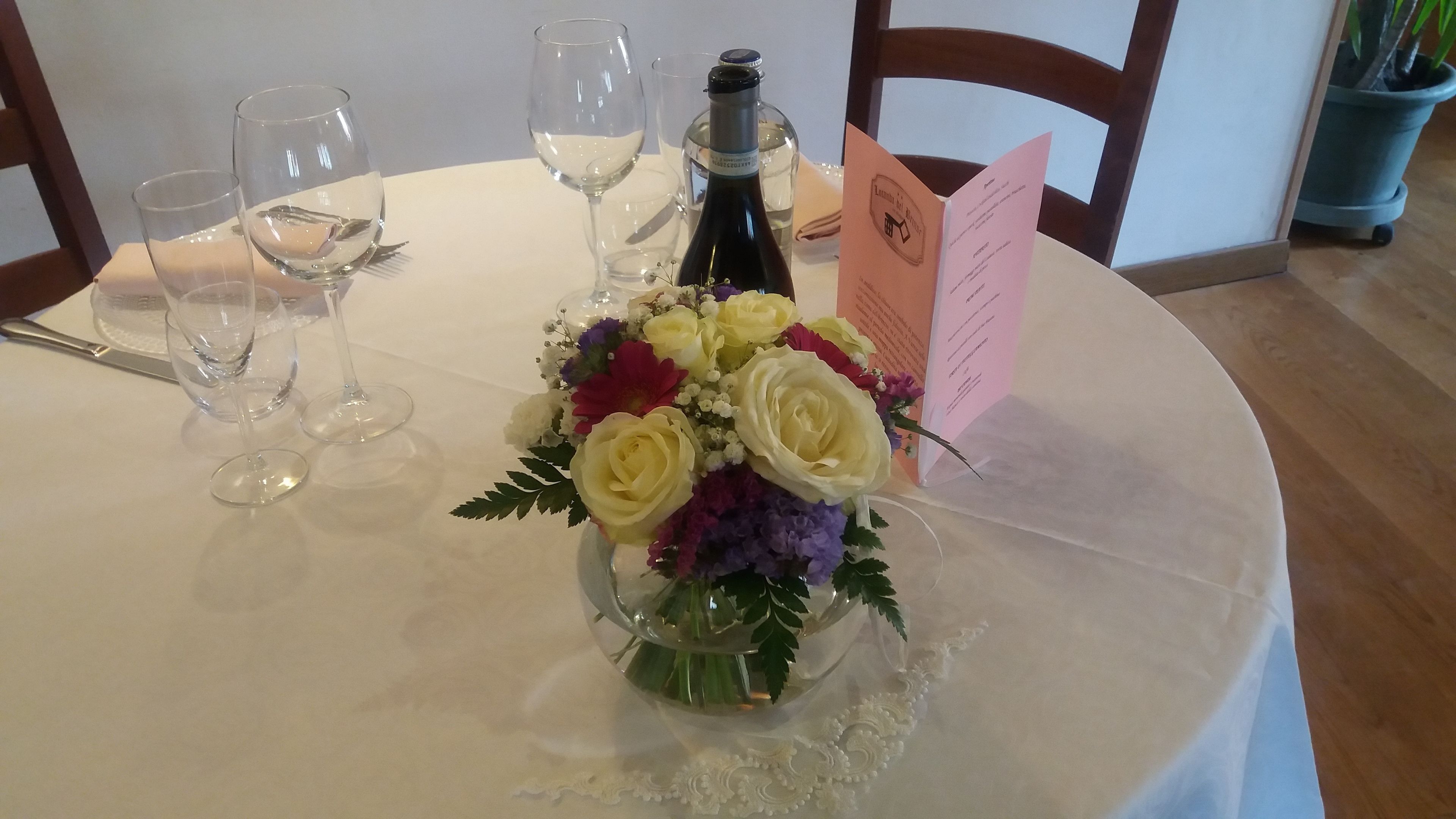 A table with a bottle of wine, a floral arrangement, and a menu.