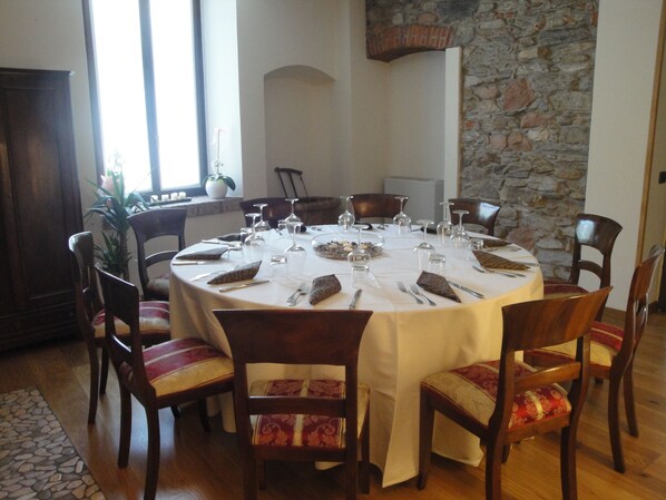 A round dining table set for six with chairs, a stone wall, and a window with natural light. - Locanda del Brinsc (Brinzio)