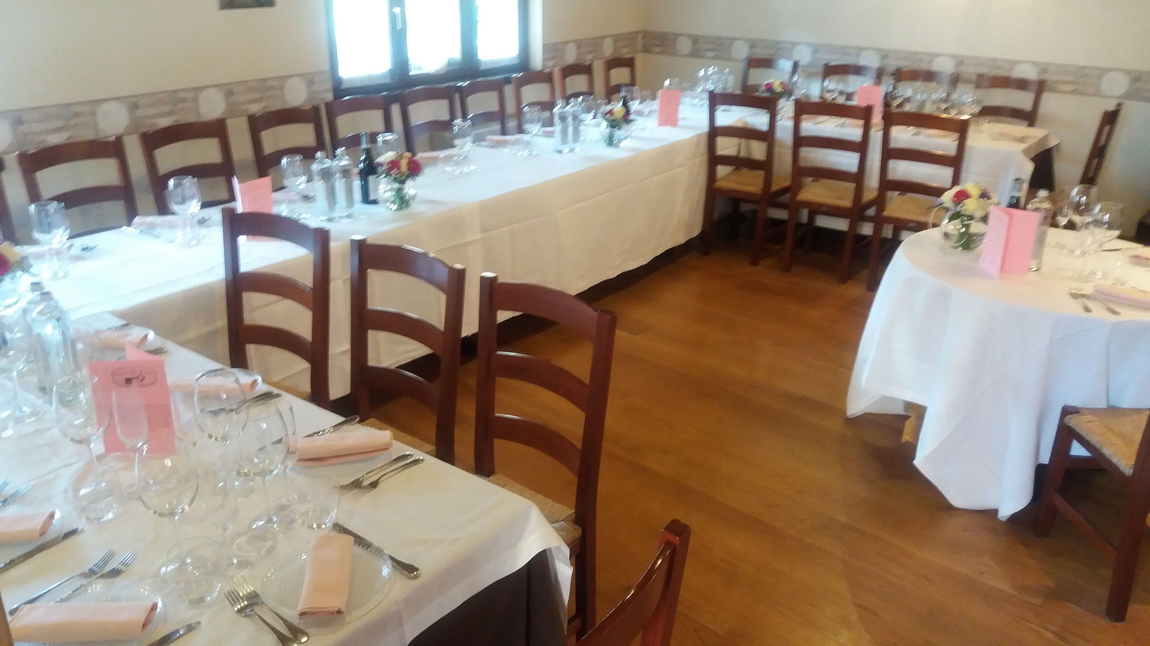 Un espace repas avec plusieurs tables dressées pour le service, chacune étant agrémentée de chaises, de couverts et de verres.
