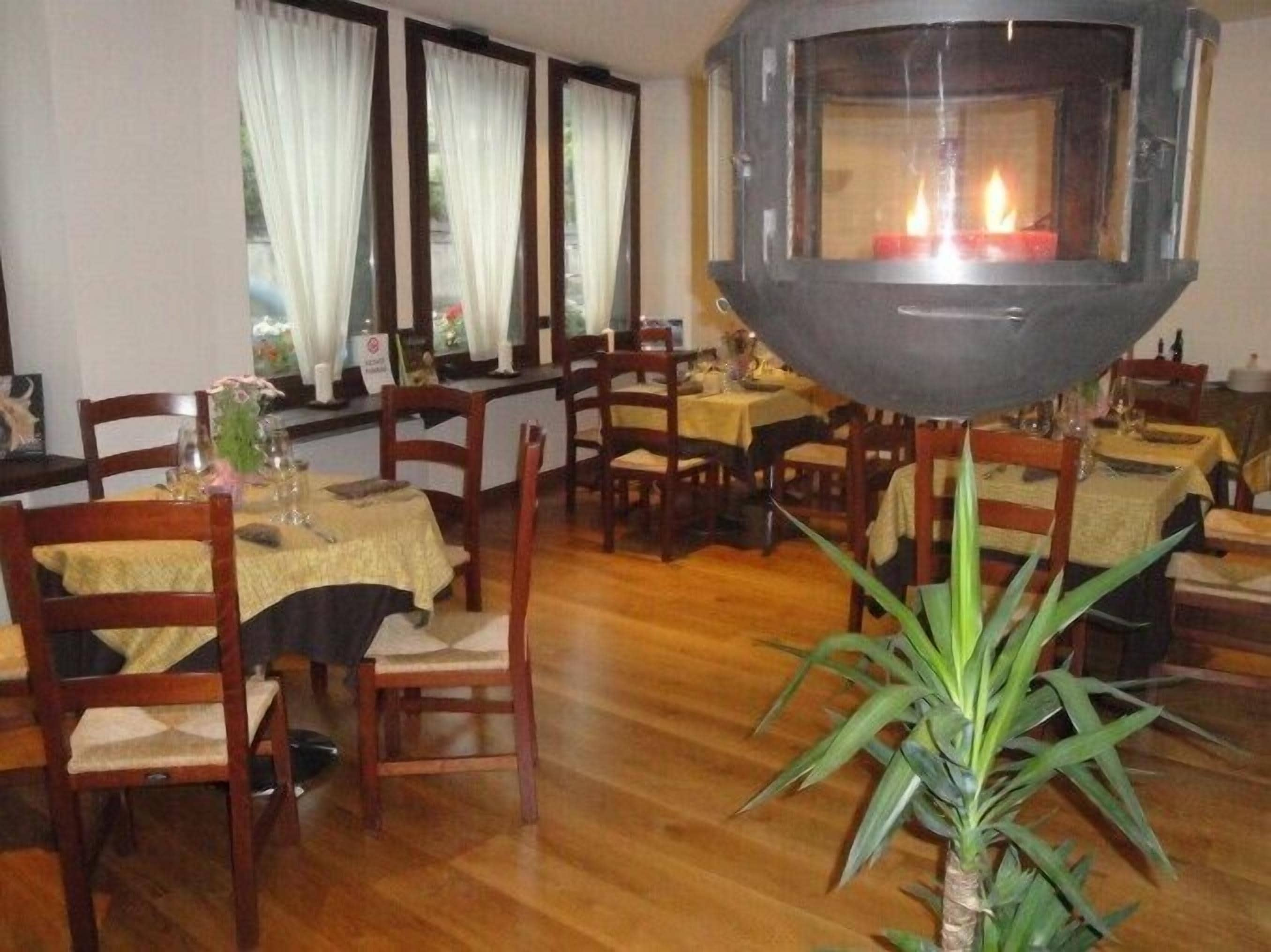 Un comedor con sillas y mesas de madera, una chimenea en el centro y una planta en maceta.