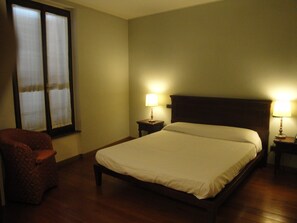 A hotel room with a bed, two bedside tables with lamps, a chair, and a window with curtains. - Locanda del Brinsc (Brinzio)