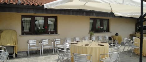 Un patio al aire libre con suelo de piedra, sillas de metal y una mesa redonda con mantel amarillo.