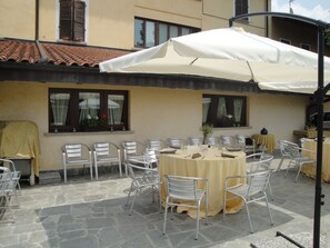 An outdoor patio with stone flooring, metal chairs, and a round table with a yellow tablecloth. - Locanda del Brinsc (Brinzio)