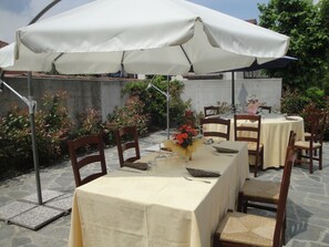 Un área de comedor al aire libre con mesas cubiertas por toldos blancos, rodeada de suelo de piedra y sillas de madera.