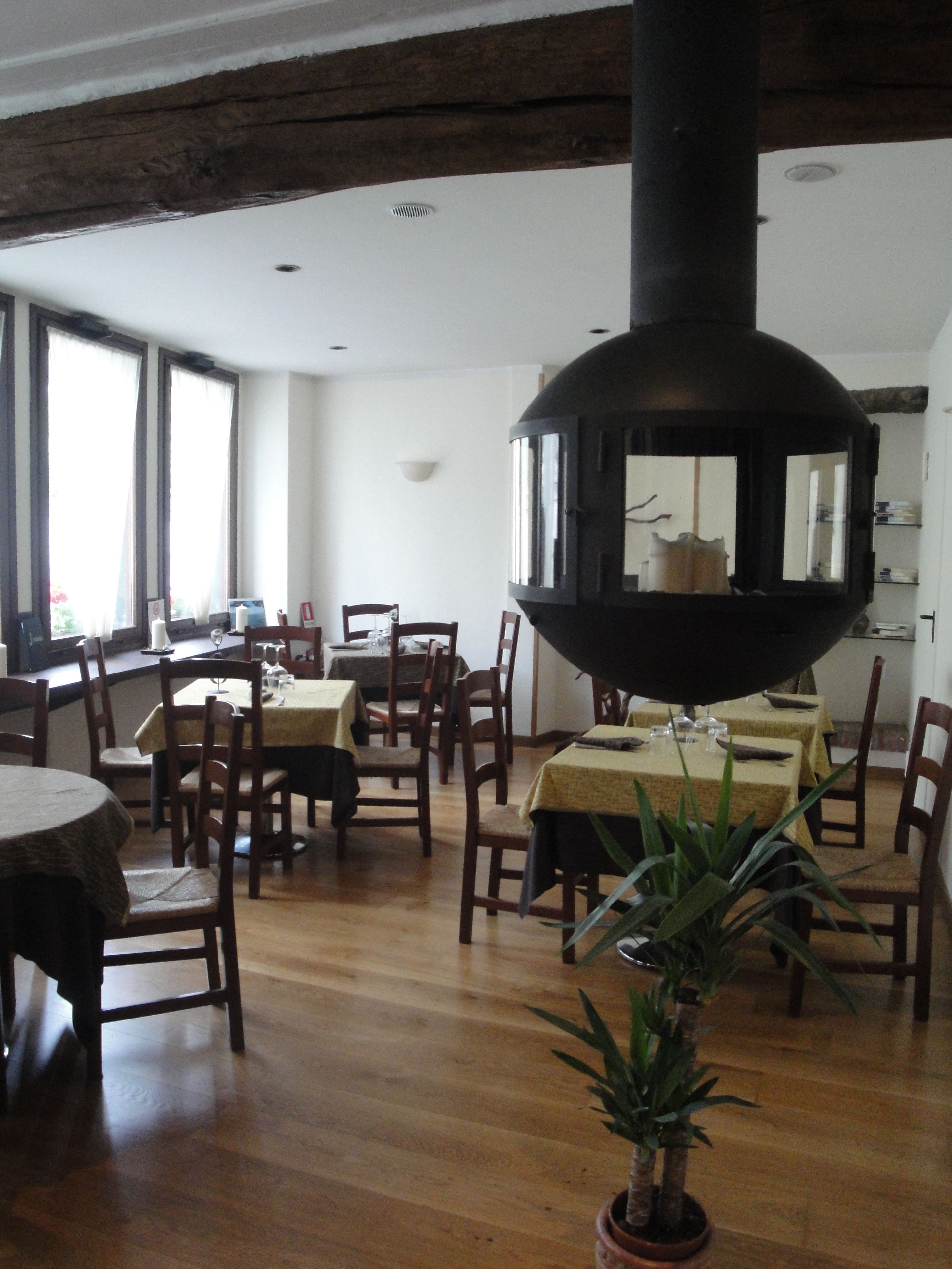 A dining area with wooden tables and chairs, a large black spherical object in the center, and a potted plant.