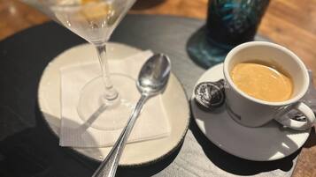 Ein Dessert in einer Glaskugel, ein Löffel, eine Tasse Kaffee und ein Glas Wasser auf einem Tisch.
