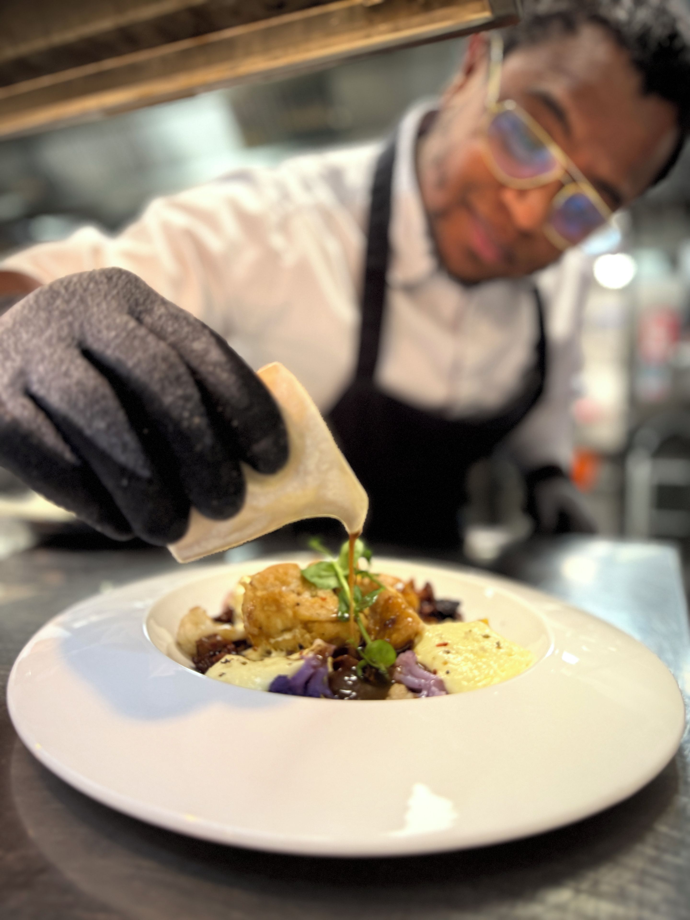 A person pouring sauce onto a dish with various food items.