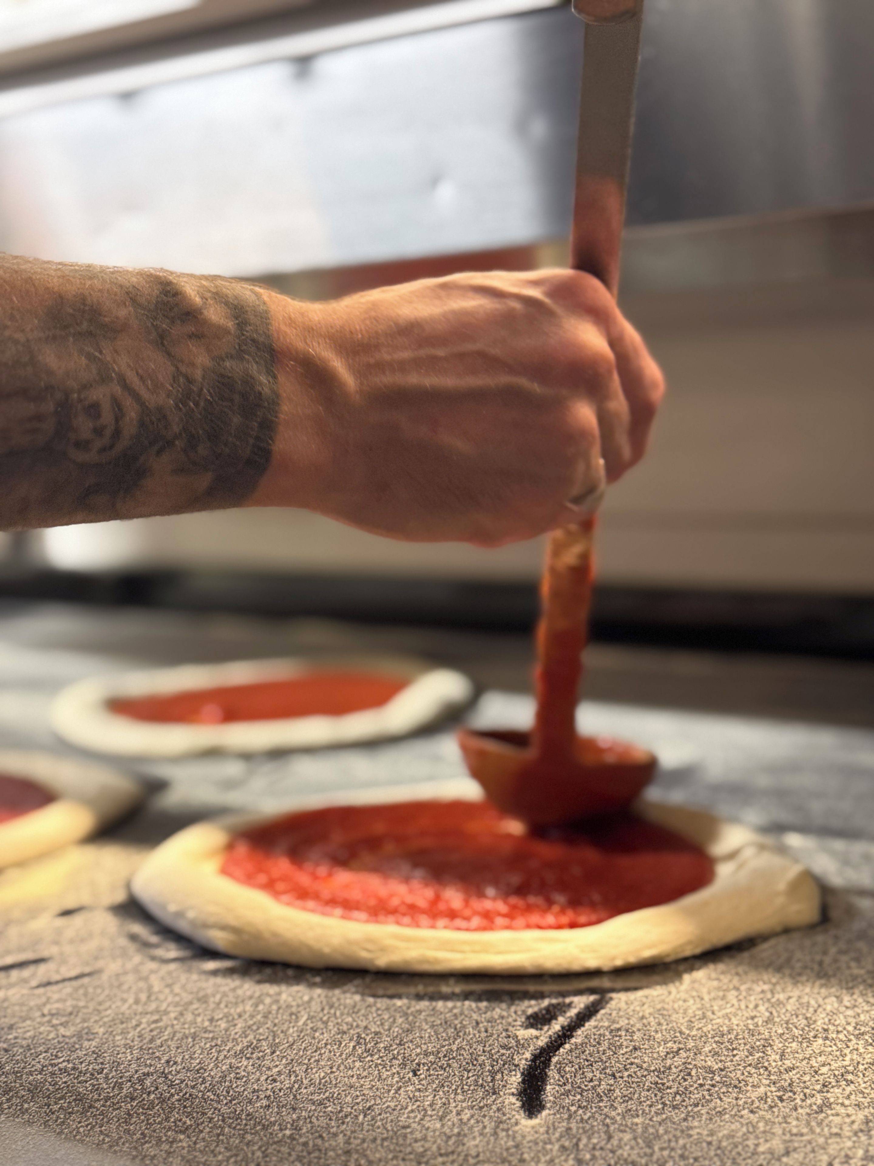 Une personne qui étale de la sauce tomate sur une pâte à pizza.