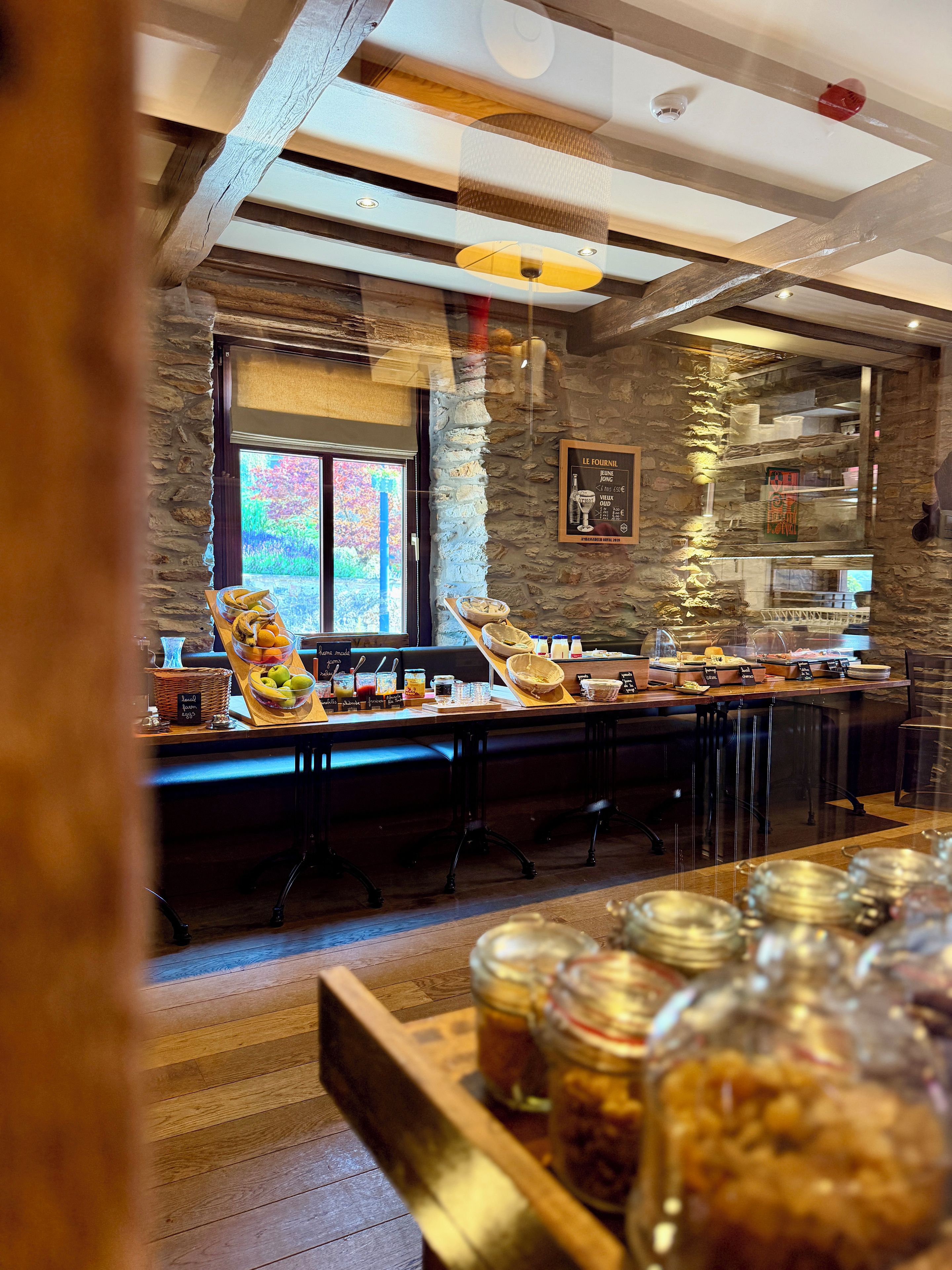Zona de desayuno buffet con pared de piedra, ventana con vistas y diversas opciones de comida.