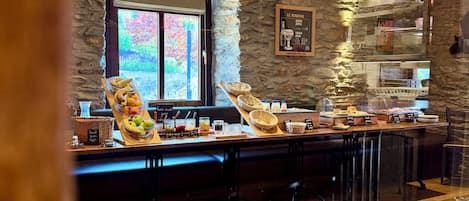 Un espace buffet pour le petit-déjeuner agrémenté d’un mur en pierre, d’une fenêtre offrant une vue agréable et de différents plats exposés.