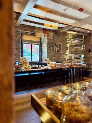 Un espace buffet pour le petit-déjeuner agrémenté d’un mur en pierre, d’une fenêtre offrant une vue agréable et de différents plats exposés.