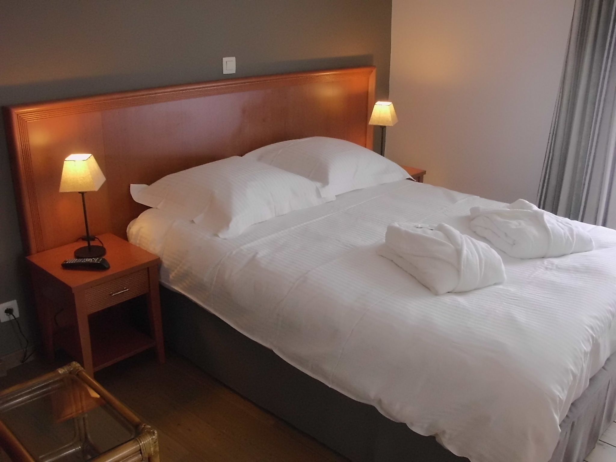 A neatly made bed with white linens, a wooden headboard, and two bedside lamps.
