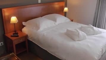 A neatly made bed with white linens, a wooden headboard, and two bedside lamps.