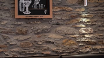 Un menu encadré accroché à un mur de pierre, un canapé en cuir noir et un coin bar avec des tabourets.