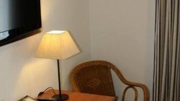 Ein Hotelzimmer mit einem Holztisch, einer Lampe, einem Sessel, einem an der Wand befestigten Fernseher und einem Vorhang.