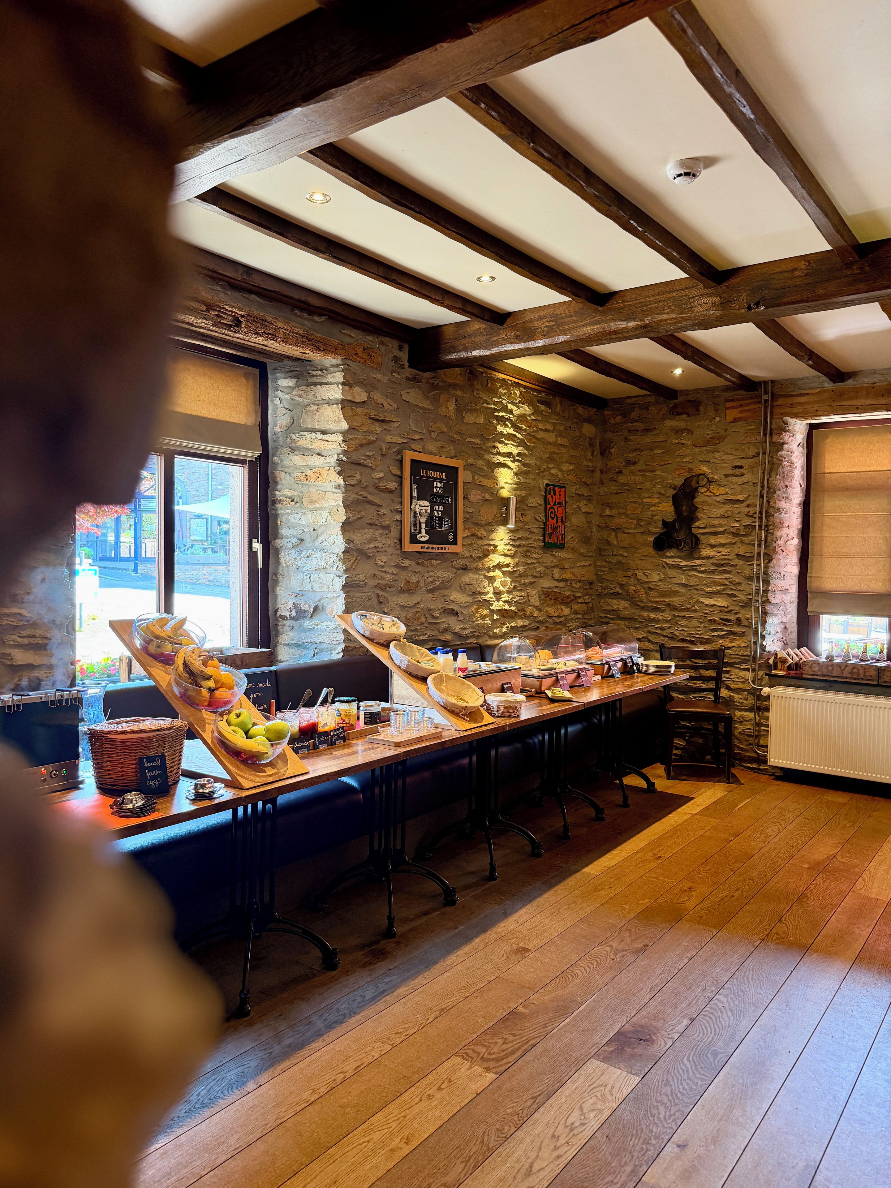 A restaurant with a long wooden table set for breakfast, stone walls, and a view through the window.