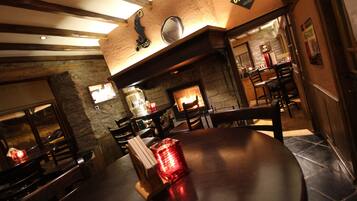 A cozy restaurant interior with a stone fireplace, wooden beams, and a round table with chairs.