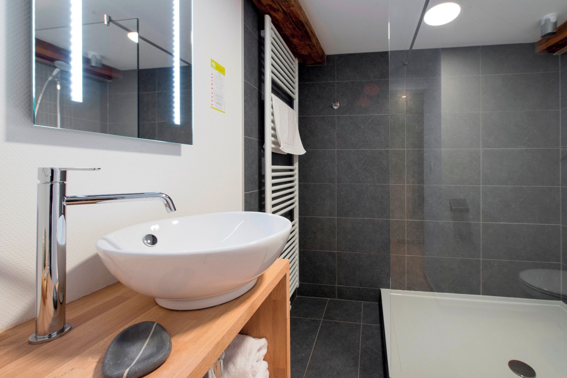 Une salle de bain moderne avec un lavabo blanc, un miroir, une étagère en bois et un espace douche.