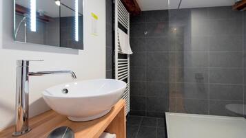 Une salle de bain moderne avec un lavabo blanc, un miroir, une étagère en bois et un espace douche.