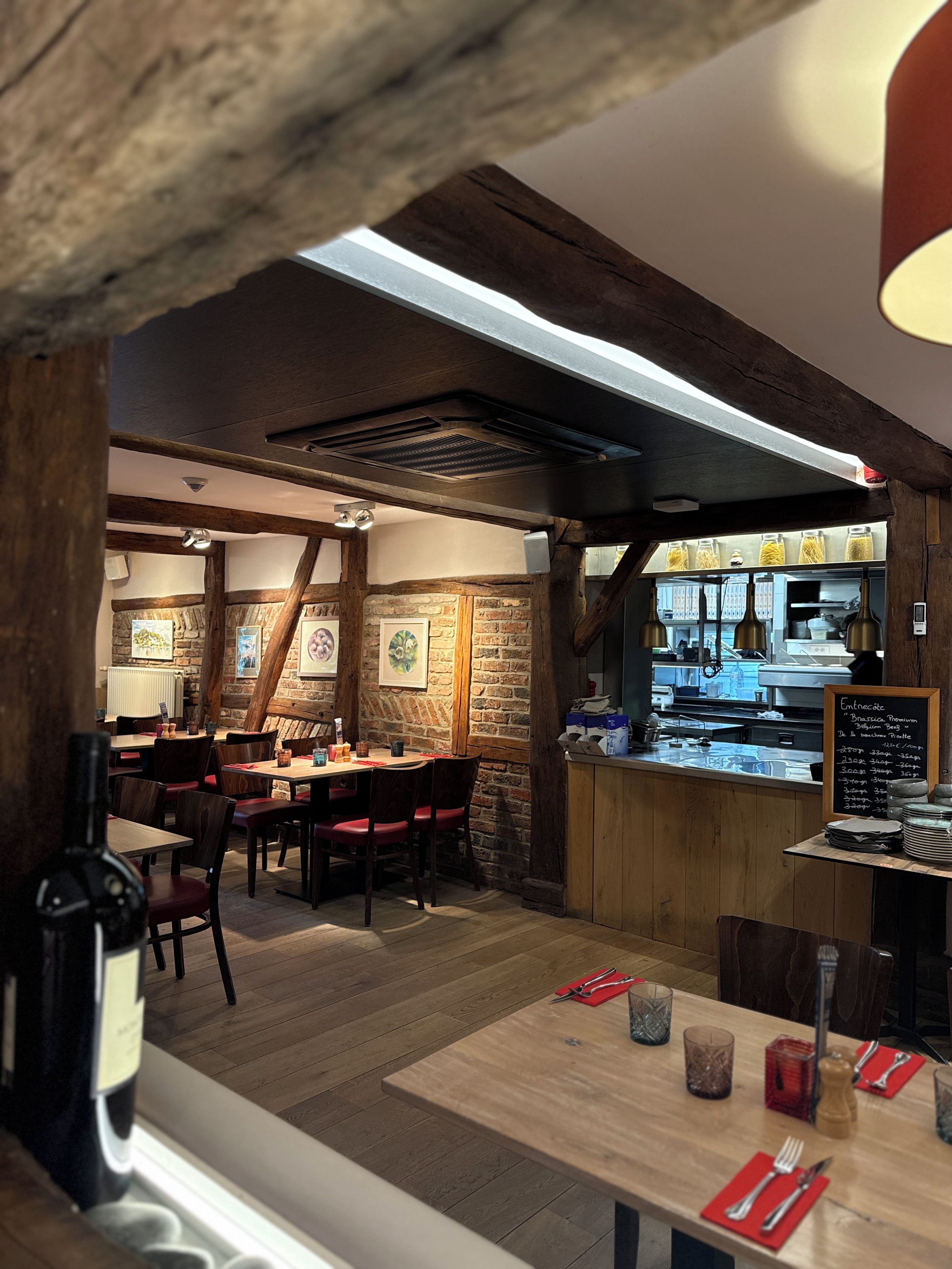 L’intérieur d’un restaurant avec des poutres en bois, des murs en briques et un coin bar doté d’un tableau noir servant de menu.