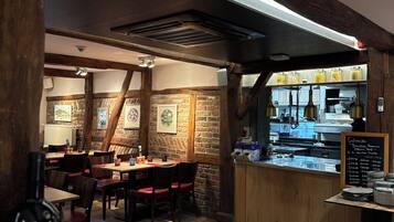 L’intérieur d’un restaurant avec des poutres en bois, des murs en briques et un coin bar doté d’un tableau noir servant de menu.